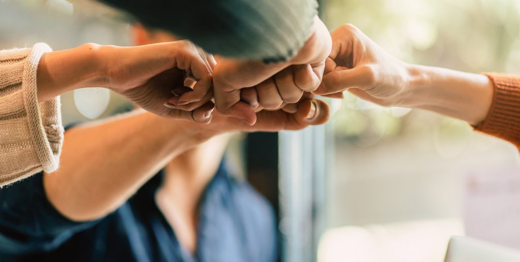 Plusieurs personnes en cercle réunies par leur poing